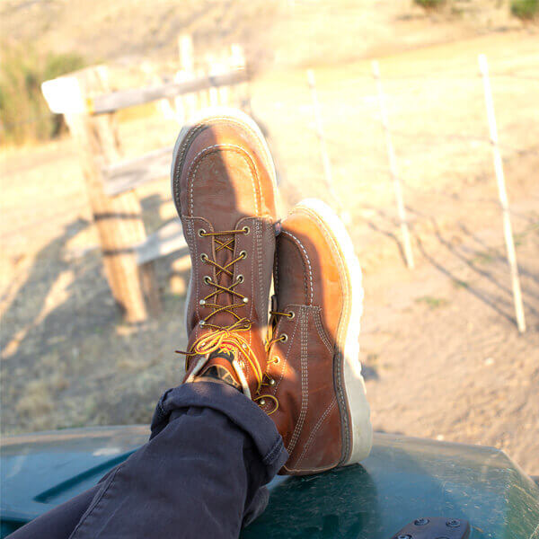 Image of American Heritage 6" tobacco moc toe with a Maxwear wedge boot on a person sitting on the hood of a vehicle
