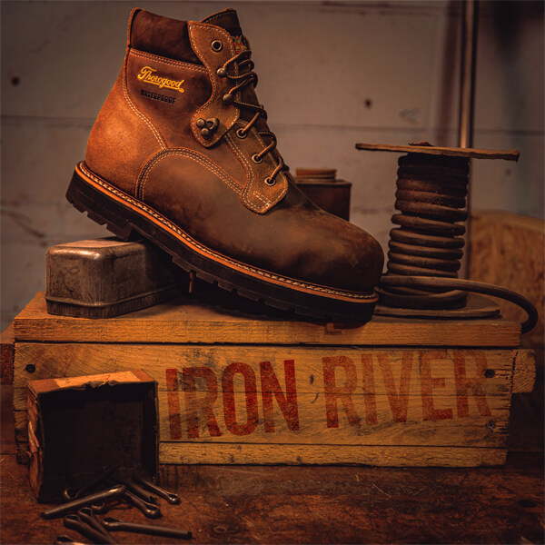 Image of the iron river series black sole boot next to some old wire and tools on a box